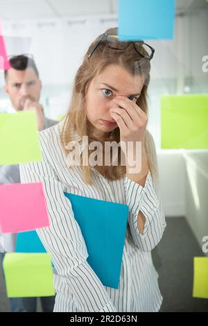Frustrierte Frau mit Haftnotizen und Aufgaben am Fenster Stockfoto
