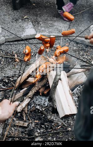 Dicke Würstchen auf Metallspießen über einem Feuer. Stockfoto