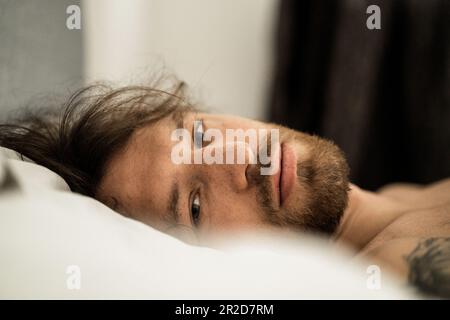 Der gutaussehende Mann im Bett wacht nach dem Schlafen auf und beginnt einen neuen Tag. Stockfoto