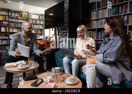 Konzeption erfolgreicher Teambildung. Drei glückliche Schüler, die ihre Hände zusammenbrachten, fertig waren mit der Vorbereitung ihres Projekts, saßen im Buchsto Stockfoto