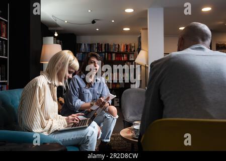 Konzeption erfolgreicher Teambildung. Drei glückliche Schüler, die ihre Hände zusammenbrachten, fertig waren mit der Vorbereitung ihres Projekts, saßen im Buchsto Stockfoto