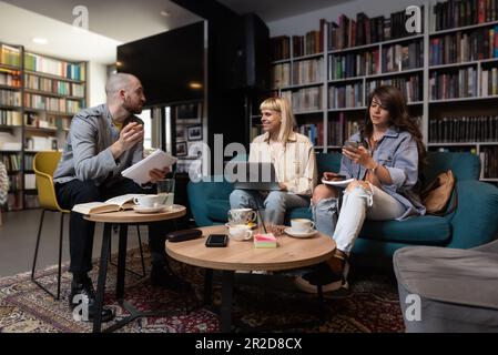 Konzeption erfolgreicher Teambildung. Drei glückliche Schüler, die ihre Hände zusammenbrachten, fertig waren mit der Vorbereitung ihres Projekts, saßen im Buchsto Stockfoto