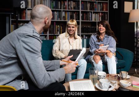 Konzeption erfolgreicher Teambildung. Drei glückliche Schüler, die ihre Hände zusammenbrachten, fertig waren mit der Vorbereitung ihres Projekts, saßen im Buchsto Stockfoto