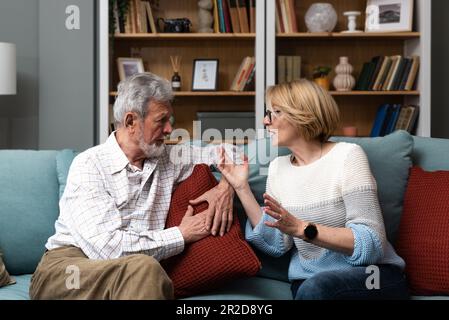 Ein gereiztes Paar mittleren Alters oder Seniorenpaar hat zu Hause harte Debatten, sitzt auf dem Sofa und streitet, verärgerte Frau, die mit einem wütenden Mann spricht, reife Ehepartner schon Stockfoto