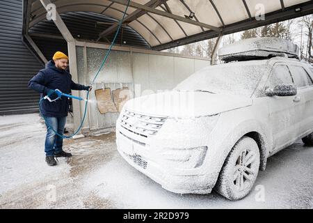 Mann wäscht bei kaltem Wetter einen amerikanischen SUV mit Dachgepäckträger. Stockfoto