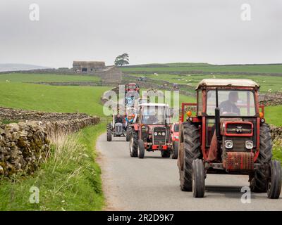 Ein Traktor fährt auf einer Straße über Settle, Yorkshire Dales, Großbritannien. Stockfoto