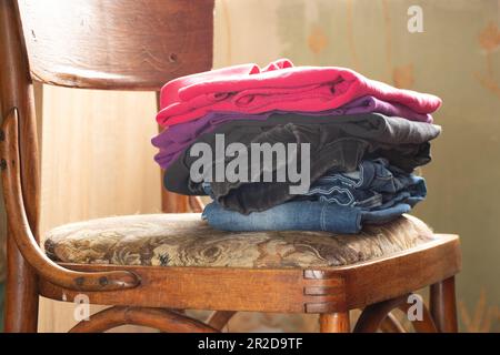 Ein Stapel gefalteter, sauberer Kleidung liegt auf einem Stuhl im Schlafzimmer in der Nähe des Fensters, Kleidung Stockfoto