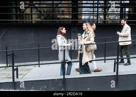 Kurze Einweisung vor dem Meeting. Eine Gruppe von fröhlichen jungen, erfolgreichen Geschäftsleuten, die sich beim Spaziergang im Freien unterhalten. Experten für Büromitarbeiter Stockfoto