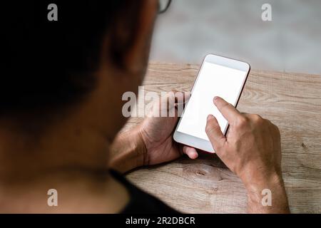 Hand eines Mannes, der sein Smartphone mit einem leeren weißen Bildschirm auf dem Schreibtischholz bei der Arbeit zu Hause berührt, Kopierbereich, verschwommener Hintergrund. Stockfoto