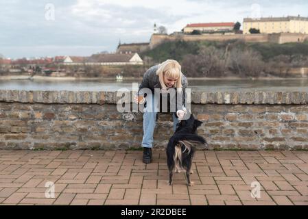 Ein junges Mädchen geht mit ihrem Adoptivhund nach draußen, den sie aus einem Tierheim rettete, und trinkt Kaffee zum Mitnehmen. Zusammen genießen sie eine gute Zeit Stockfoto