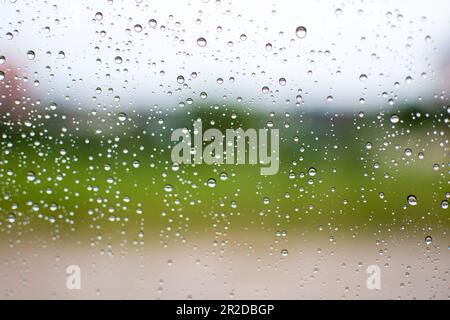 Helle Regentropfen auf Autoglas, abends nach der Arbeit, auf dem Parkplatz, Nahaufnahme eines Fotos, Boden- und Grasunschärfe im Hintergrund, Bild ist die Landschaft und Stockfoto