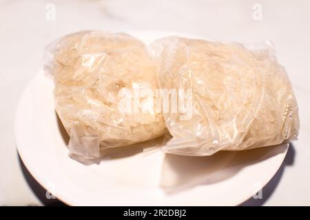 Glutinous Reis ist das thailändische Essen, für ISan lokal verpackt mit Plastik und hat einen Wassertropfen von einem Koch und wird auf einen weißen Teller auf dem Tischfoto gestellt Stockfoto