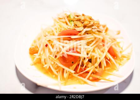 Der Papayasalat hat Pfeffer, getrocknete Garnelen und Tomaten ist das thailändische Essen, für einen lokalen und würzigen Geschmack. Auf dem Tisch ist ein weißes Foto zu sehen Stockfoto