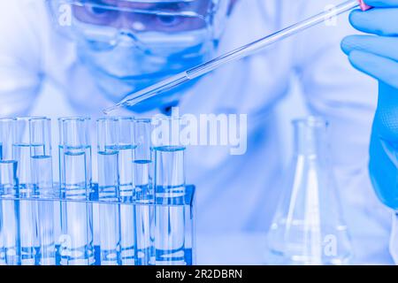 Ein männlicher Wissenschaftler, der Schutzbrille und Handschuhe trägt, tropft Chemikalien, um einen Impfstoff zu testen. Biochemiker führen DISG-Experimente durch Stockfoto
