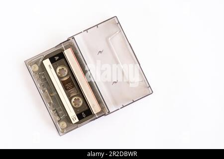 Ein Band in einer Kassette, das die Technologie des 90s zur Aufnahme von Musik oder Geräuschen ist, wird auf einen weißen Tisch gelegt, Nahaufnahme, selektiv fokussiert, weiß Stockfoto