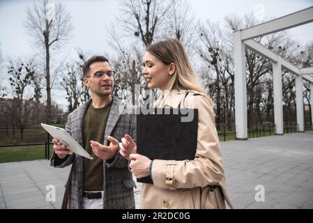 Junge Geschäftsleute Geschäftsmann und Geschäftsfrau gehen vom Bürogebäude zum Gebäude zwischen Meetings, wo sie Mitarbeiter zu besseren und besseren Schulen Stockfoto