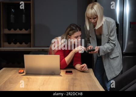 Zwei lächelnde weibliche Geschäftsinhaber und Partner, die sich auf ein Online-Meeting mit einem Laptop vorbereiten. Zwei zufriedene Geschäftsleute, die sich mit ihrer globalen cli verbinden Stockfoto
