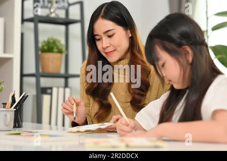 Süßes kleines asiatisches Mädchen, das mit ihrer Mutter im Wohnzimmer malt. Familienheim Freizeitkonzept Stockfoto