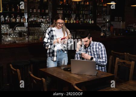 Zwei verschiedene Unternehmer veranstalten ein Team Meeting in ihrem eleganten Coffee Shop. Barista und Café-Besitzer besprechen Arbeitszeitplan und Menü auf Mobile oder Compute Stockfoto