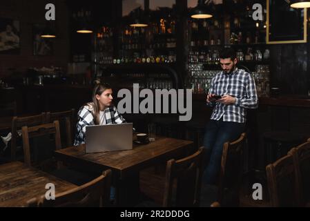 Zwei verschiedene Unternehmer veranstalten ein Team Meeting in ihrem eleganten Coffee Shop. Barista und Café-Besitzer besprechen Arbeitszeitplan und Menü auf Mobile oder Compute Stockfoto