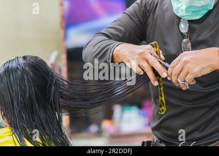 Professioneller Mann Friseur trägt Gesichtsmaske mit Schere und Haarschneider Klientin Frau im Innenbereich Salon, Mann machen Business Haarpflege hat Werkzeug Haarschnitt Stockfoto