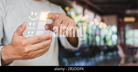 Ein Kundenmann, der mit dem Finger auf einen virtuellen Bildschirm zeigt, zeigt auf das Symbol für ein glückliches Smiley, um Zufriedenheit mit dem Service zu zeigen. Zufriedenheitsumfrage, und Stockfoto