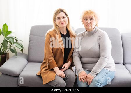 Nahaufnahme gealterte Mutter Erwachsene Tochter, die drinnen auf dem Sofa sitzt und lächelt und für die Kamera posiert, fühlt sich glücklich an, Zeit miteinander zu verbringen, Concept Stockfoto