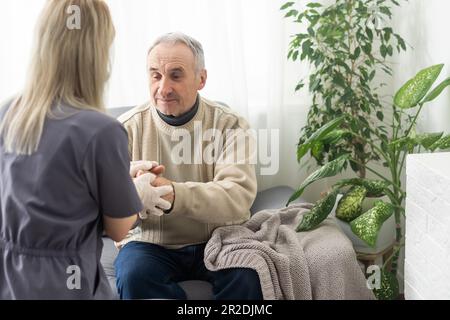 Fürsorgliche Krankenschwester spricht mit altem Patienten hält seine Hand sitzen im Wohnzimmer bei Homecare Besuch bieten psychologische Unterstützung zuhören klagt Empathie zeigen Stockfoto