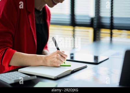 Zugeschnittenes Bild einer Mitarbeiterin, die wichtige Notizen macht, einen täglichen Termin plant und eine Geschäftsreise in ein Tagebuch schreibt Stockfoto