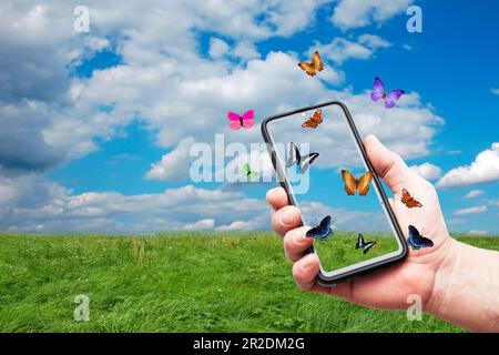 Die Hand hält ein Smartphone, mit Schmetterlingen, die es umherfliegen Stockfoto