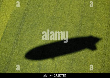 19. Mai 2023, Nordrhein-Westfalen, Mülheim an der Ruhr: Der Zeppelin NT Bodensee wirft seinen Schatten auf ein Rapsfeld. Am Flughafen Essen/Mülheim wurde ein neues Luftschiff der Deutschen Zeppelin-Reederei vorgestellt, das ab Mai nächsten Jahres Besichtigungsflüge über das Ruhrgebiet und Rheinland anbietet. Foto: Federico Gambarini/dpa Stockfoto