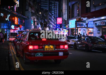 Hongkong, China - April 10 2023: Rotes Taxi in einer Straße in der Innenstadt von Mong Kok und Neonlichter Stockfoto