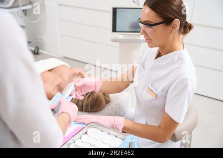 Assistent gibt ein Werkzeug für Kosmetiker in der Schutzbrille ab Stockfoto