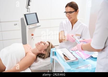 Assistentin geht Kosmetikerin in Schutzbrille für kosmetische Eingriffe Stockfoto