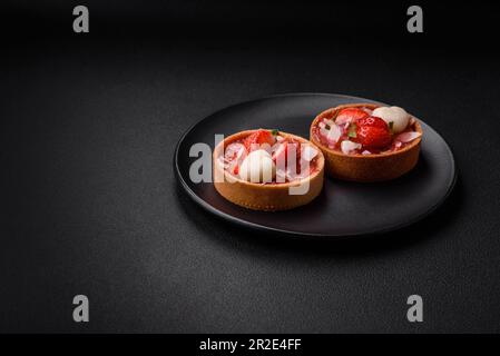 Köstliche frische süße Törtchen mit Erdbeeren und Kokosflocken auf dunklem Betonhintergrund Stockfoto