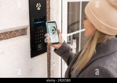 Frau, die smartlock an der Eingangstür mit einem Smartphone verriegelt. Konzept der Verwendung intelligenter elektronischer Schlösser mit schlüssellosem Zugang. Stockfoto