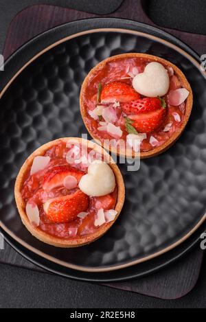 Köstliche frische süße Törtchen mit Erdbeeren und Kokosflocken auf dunklem Betonhintergrund Stockfoto