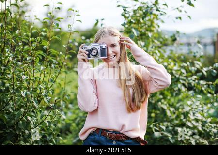 Glückliche Frau, die eine Oldtimer-Kamera in einem Garten hält, Lifestyle-Konzept. Stockfoto