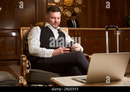 Geschäftsmann sitzt mit Smartphone in der Hotellobby Stockfoto