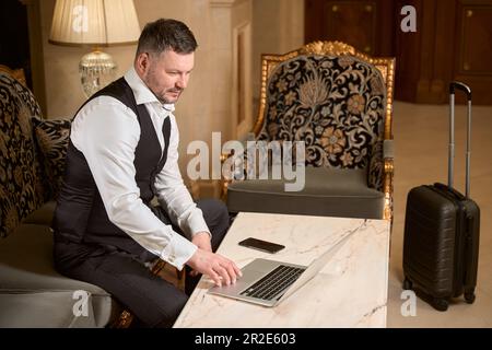 Geschäftsmann, der an einem Laptop am Tisch im Hotel arbeitet Stockfoto