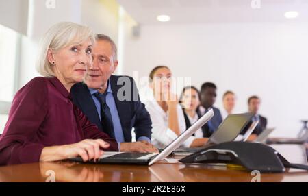 Älterer Geschäftsmann, der Geschäftsfrau während eines Geschäftstreffens zuflüstert Stockfoto