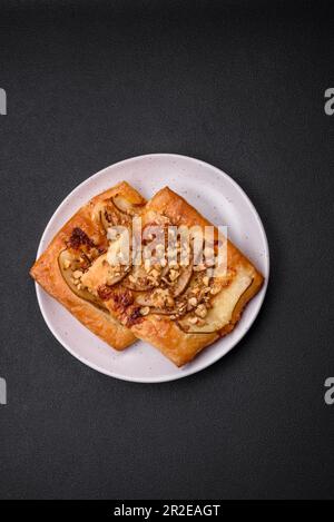 Köstlicher süßer Kuchen oder Pizza mit Birne, Brie, Honig und Nüssen auf dunklem Betonhintergrund Stockfoto