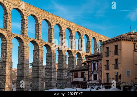 Blick auf die Plaza Azoguejo im Zentrum der Stadt. Farben des Sonnenuntergangs. Gäste, die sich in den Bars und Restaurants auf der Straße von Segovia entspannen möchten. Stockfoto