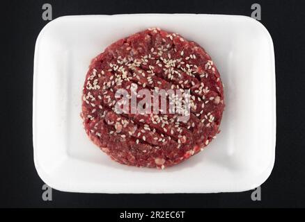 Rohe Hamburger-Pasteten mit Sesamsamen auf einem weißen Teller. Stockfoto