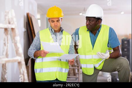 Bauherren mit Gespräch über den Arbeitsplan in der Wohnung Stockfoto