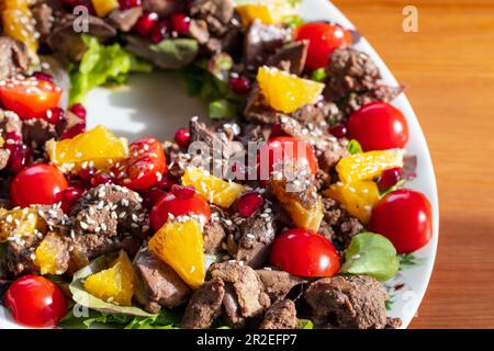 Warmer Salat mit Hühnerleber, Kirschtomaten, Orangen, Salat, Granatapfelsamen und Sesam. Nahaufnahme mit selektivem Weichzeichner Stockfoto