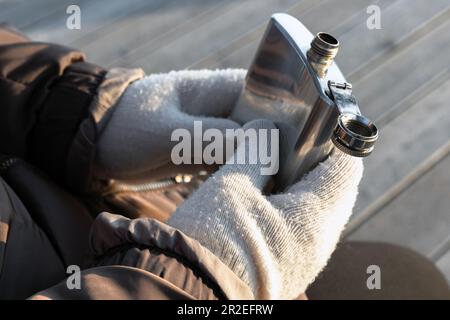 Glänzender Taschenkolben aus Stahl in den Händen eines Mannes, Außenfoto an einem kalten Tag Stockfoto