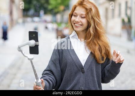 Junge rothaarige, schöne Frau, die läuft und ihr Handy benutzt Stockfoto