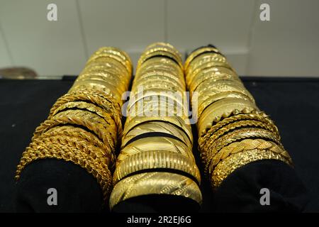 Luxuriöse goldene Armbänder, drei Reihen imitierter goldener Armbänder auf schwarzem Schmuckhintergrund. Stockfoto