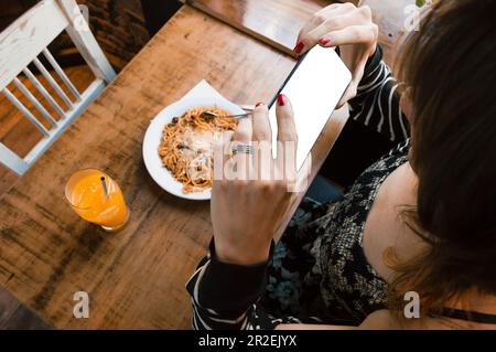 Die erste Person sieht eine Transgender-Frau, die in einem Restaurant sitzt, ein Foto mit ihrem Handy macht, das Essen, das Technologiekonzept, den Kopierraum. Stockfoto